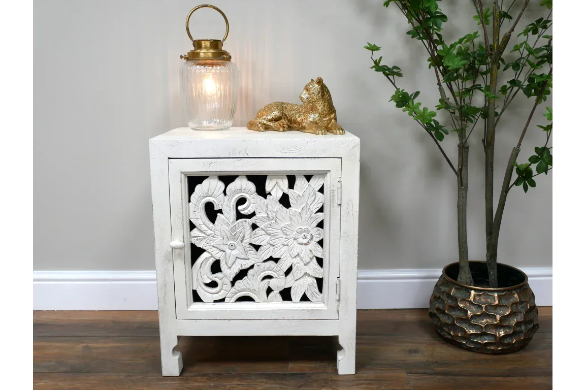 White carved wooden bedside cabinet with floral detail, styled with gold ornament and lamp