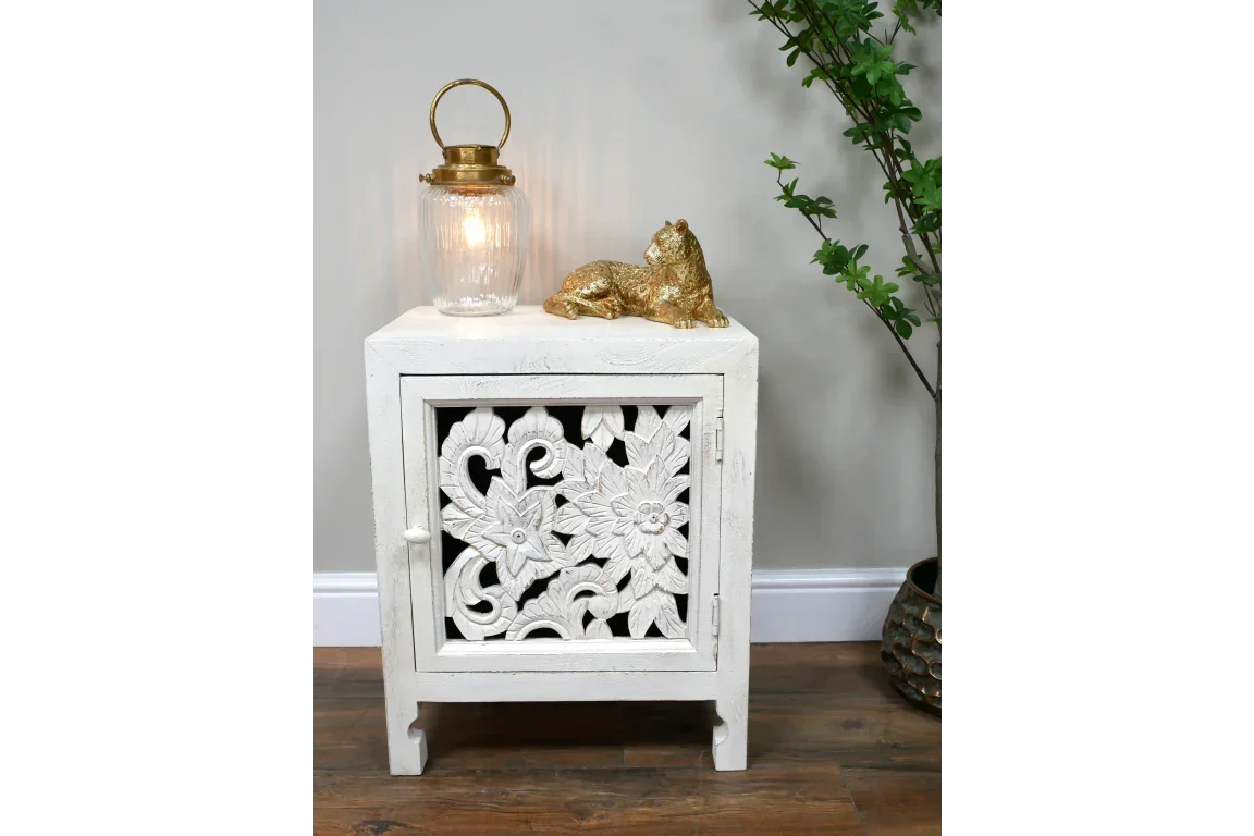 White carved wood bedside cabinet with floral door panel on wooden floor