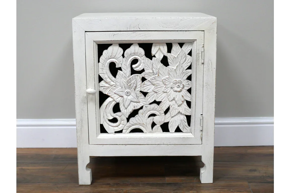 White carved wooden cabinet with floral pattern on door, shown against a pale wall