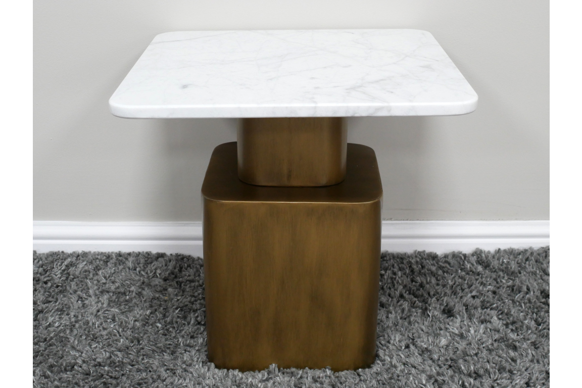 Square side table with white marble top and bronze metal base on gray shag carpet against white wall.