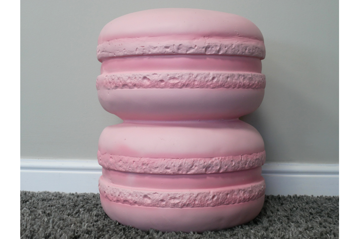 Pink resin side table shaped like two stacked macarons, front view on grey carpet and white baseboard background.