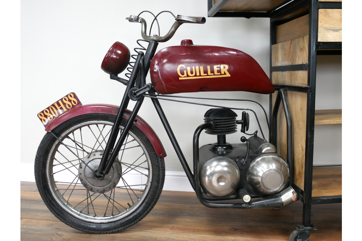 Metal and wood motorbike-shaped bar cabinet in red and black, side view, indoors on wooden floor near shelving unit.
