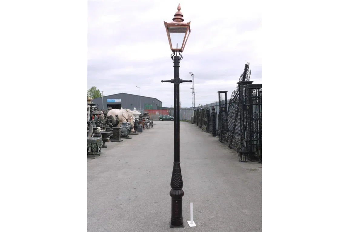 Traditional outdoor lamp post with copper lantern, black cast iron base, on paved surface