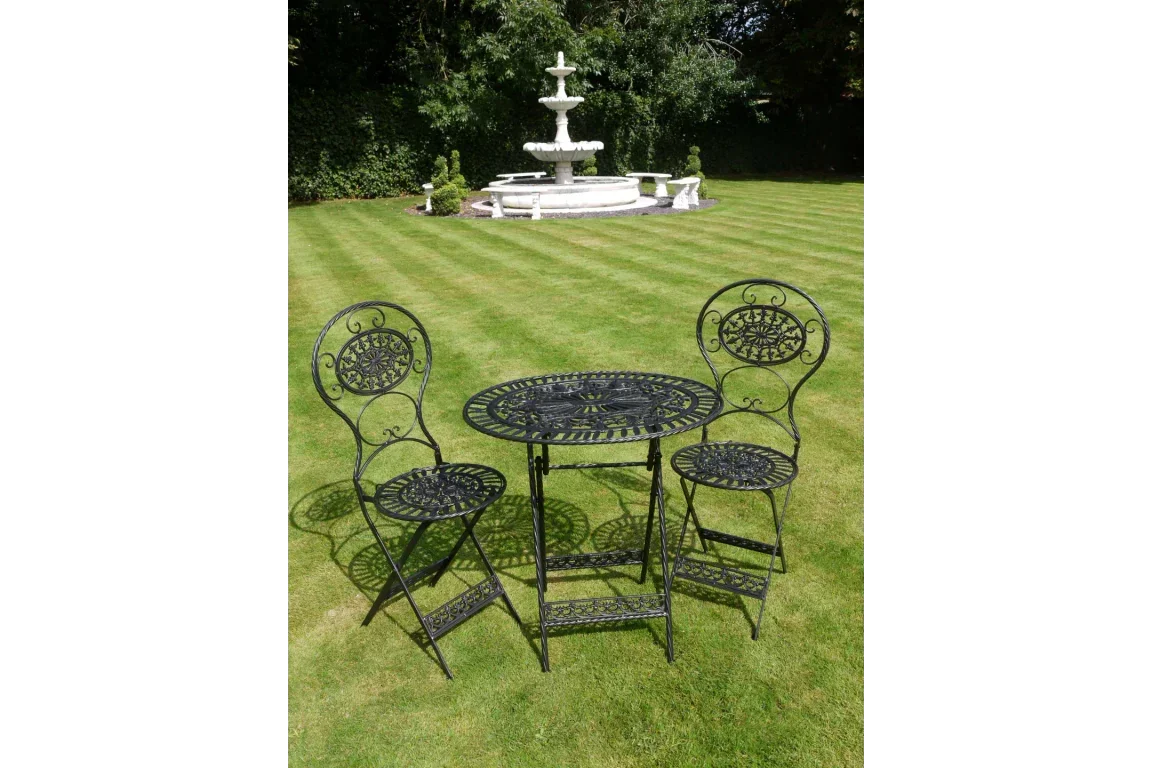 Black metal garden bistro set with round table and two chairs on lawn near fountain