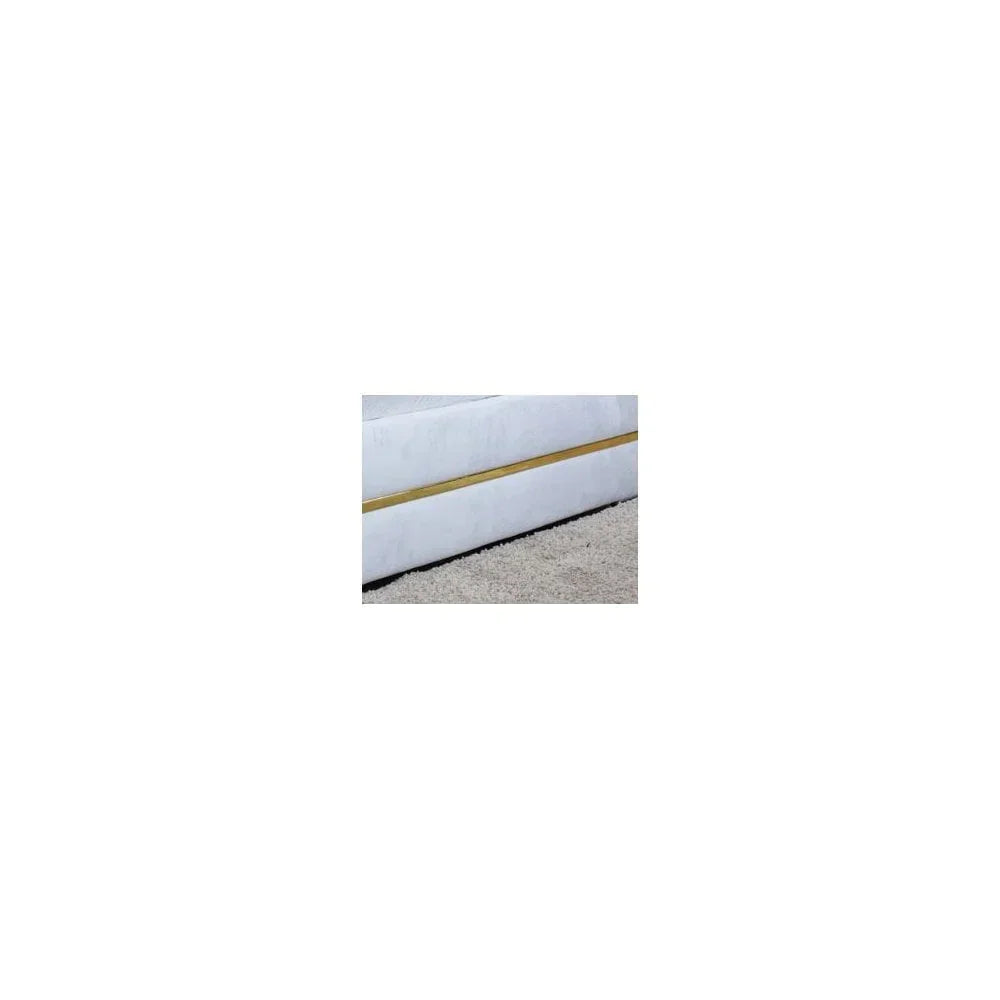 Closeup of bed base upholstered in light fabric with gold accent on beige carpet