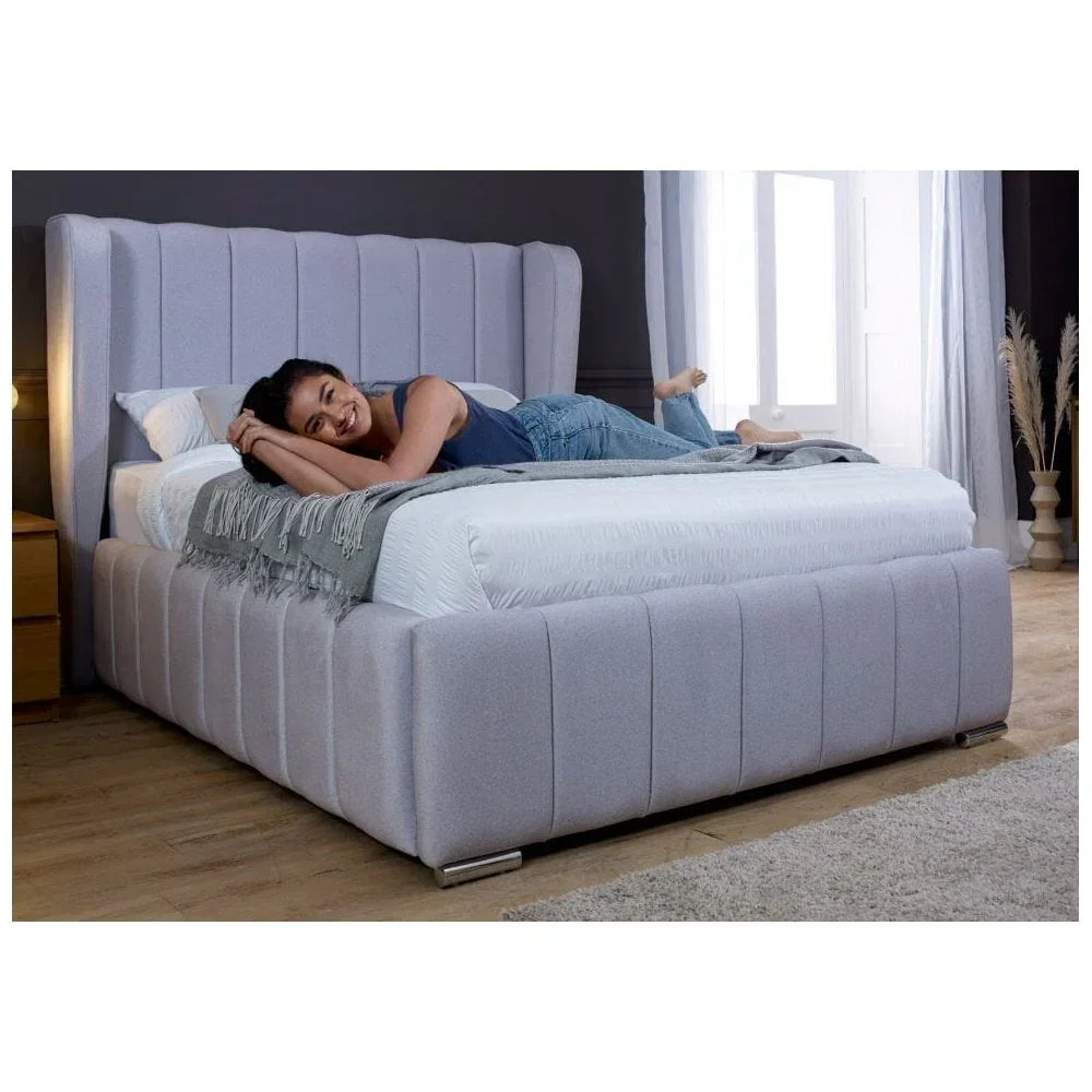 Grey upholstered bed frame with high headboard in bedroom, woman lying on mattress