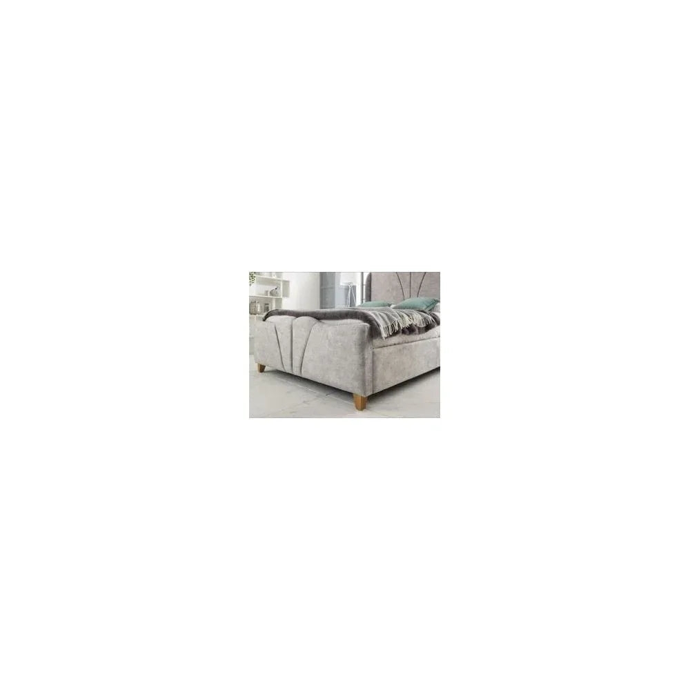 Grey velvet bed frame with wood legs and scalloped detail, footboard angle view