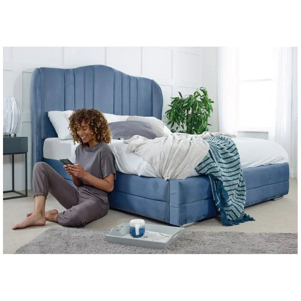 Blue upholstered bed with high headboard, blanket and tray, staged in a bright bedroom