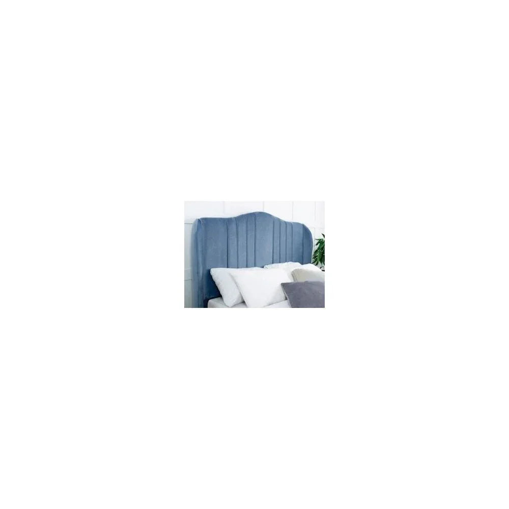Blue upholstered headboard with vertical stitching behind white bedding and pillows