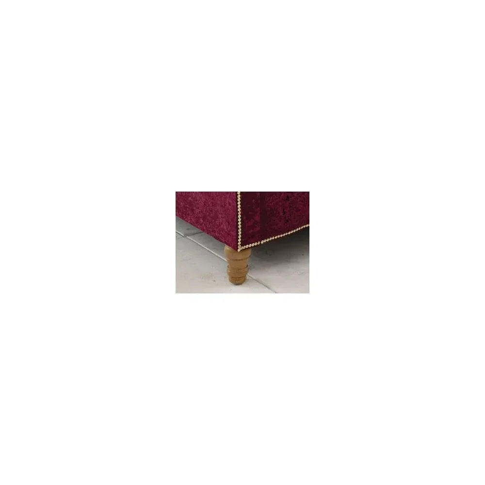 Red velvet sofa corner with gold stud trim and turned wooden leg on tiled floor