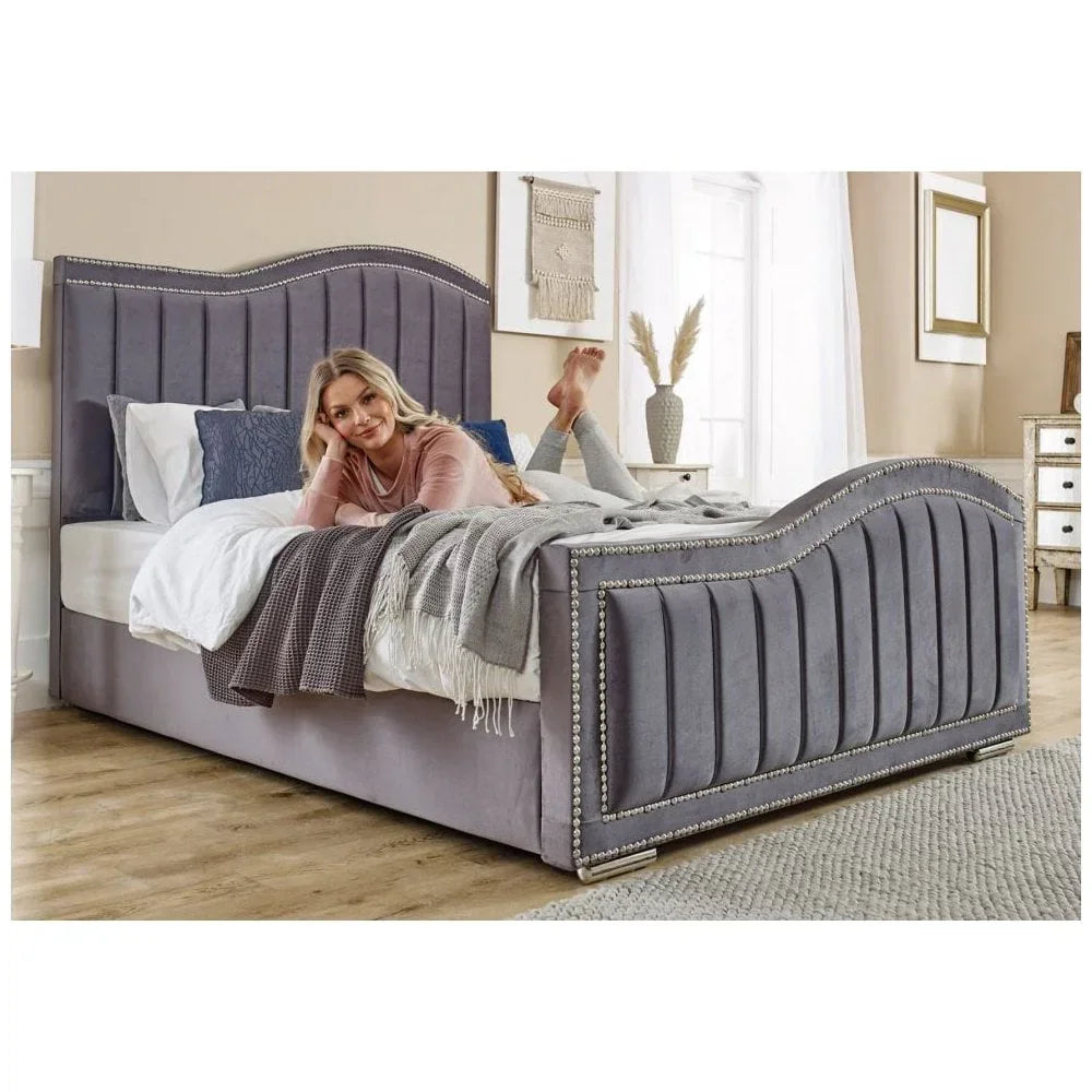 Grey velvet upholstered bed frame with silver stud trim in a bright bedroom setting