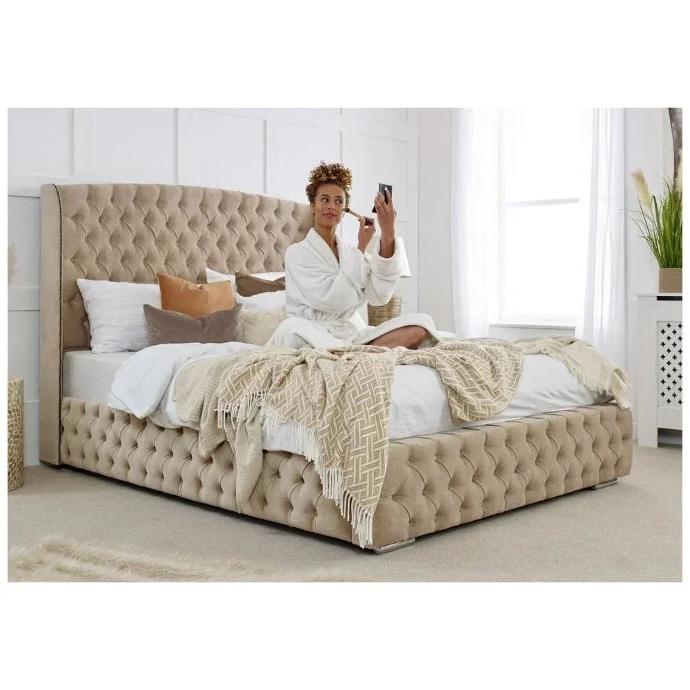 Beige upholstered bed frame with deep button tufting, woman sitting on bed applying makeup