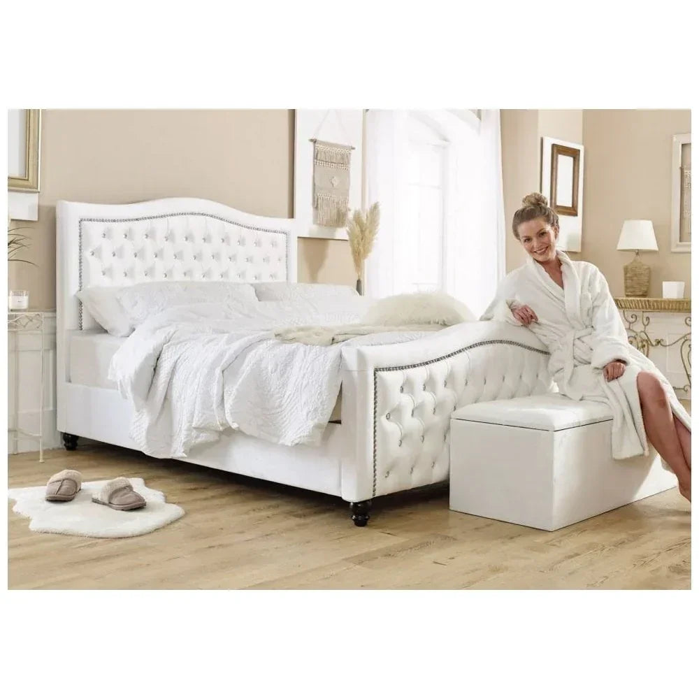 White upholstered bed with studded headboard in bright bedroom, woman seated on end bench