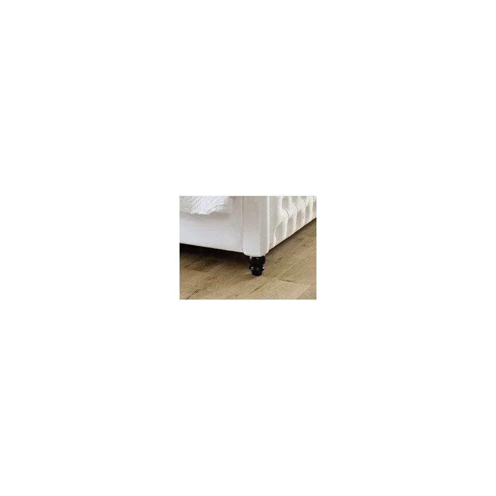 White upholstered bed frame corner with tufted side and dark wooden leg on wooden floor