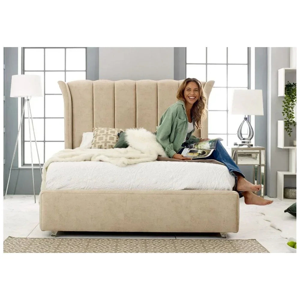 Beige upholstered bed with tall wingback headboard, woman sitting on bed holding magazine