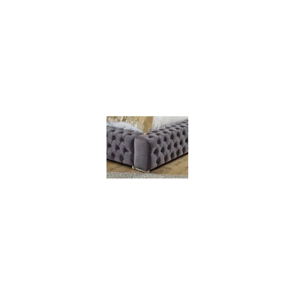 Grey velvet upholstered bed frame with deep button tufting and chrome feet on wood floor