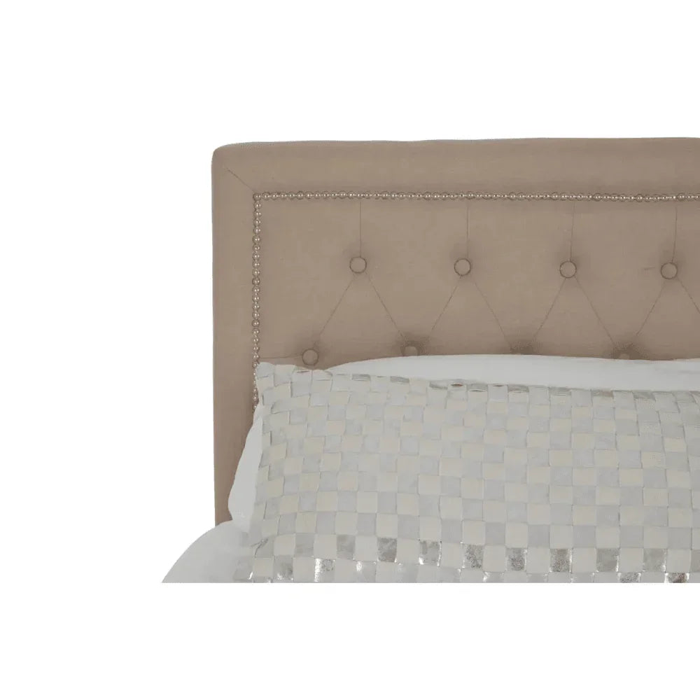 Beige upholstered bed headboard with button detailing and silver stud trim, partial pillow visible
