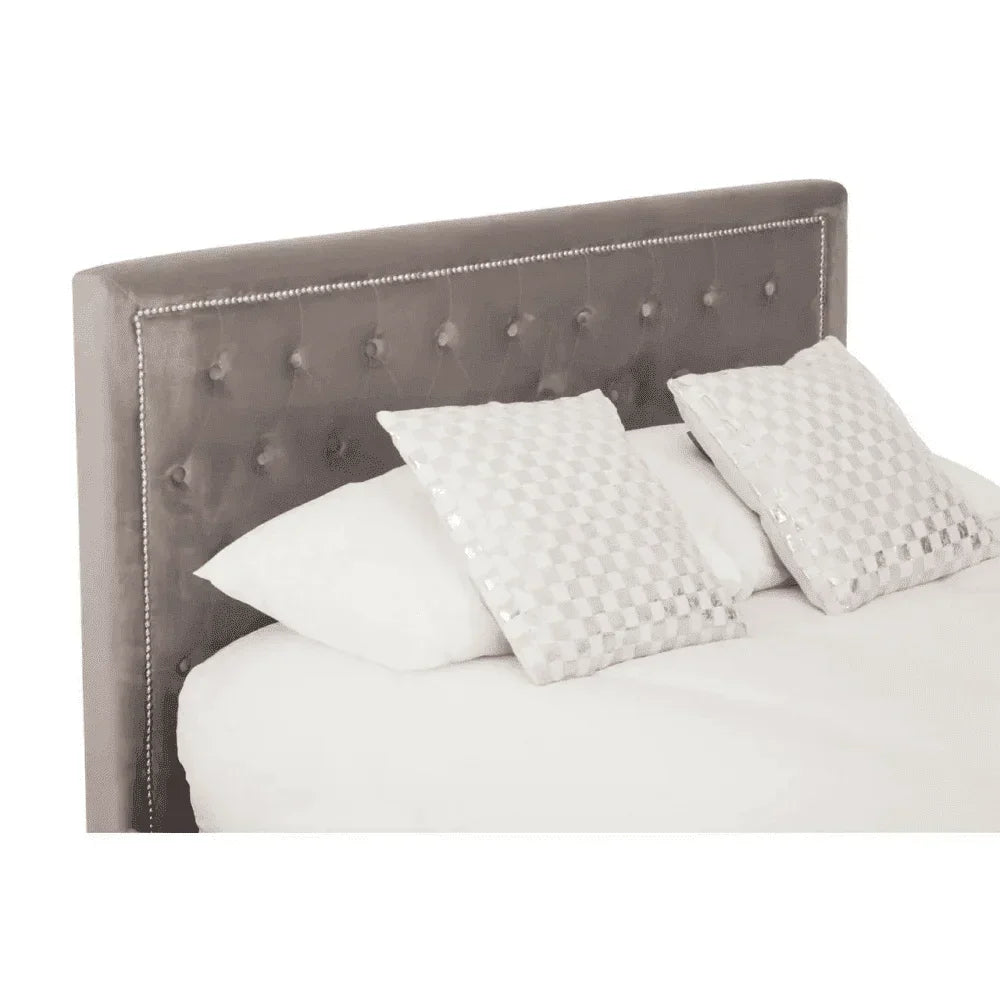 Grey upholstered bed with buttoned headboard and silver trim, two decorative pillows on top