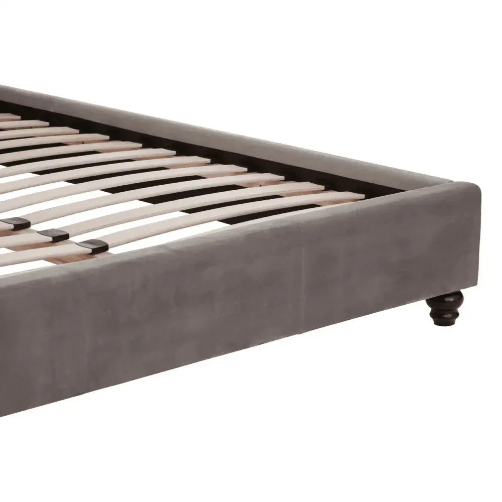 Grey upholstered bed frame with wooden slats and dark turned leg, side angle view
