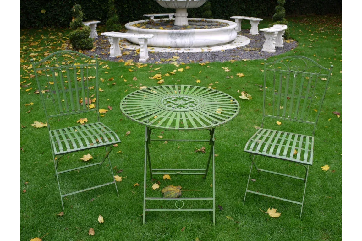 green metal garden bistro set with round table and two chairs on lawn near stone fountain