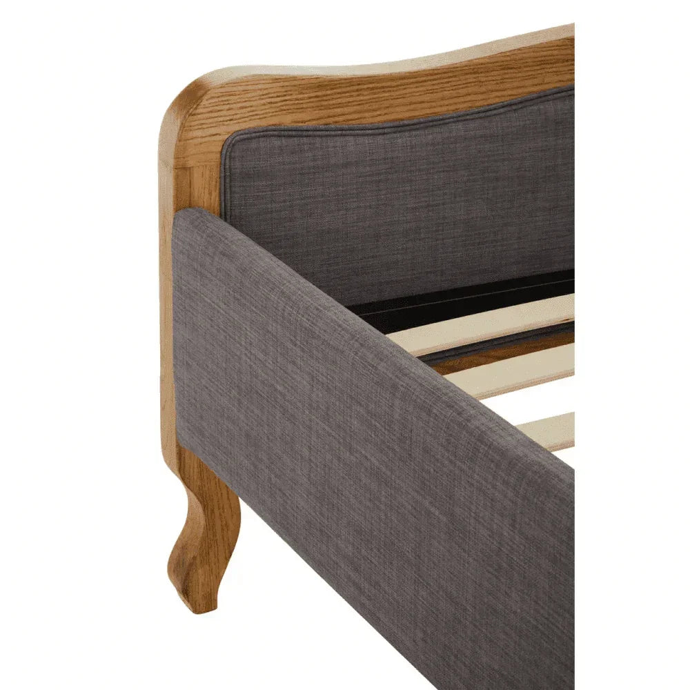 Grey fabric upholstered bed frame with oak wood detail and slatted base corner view