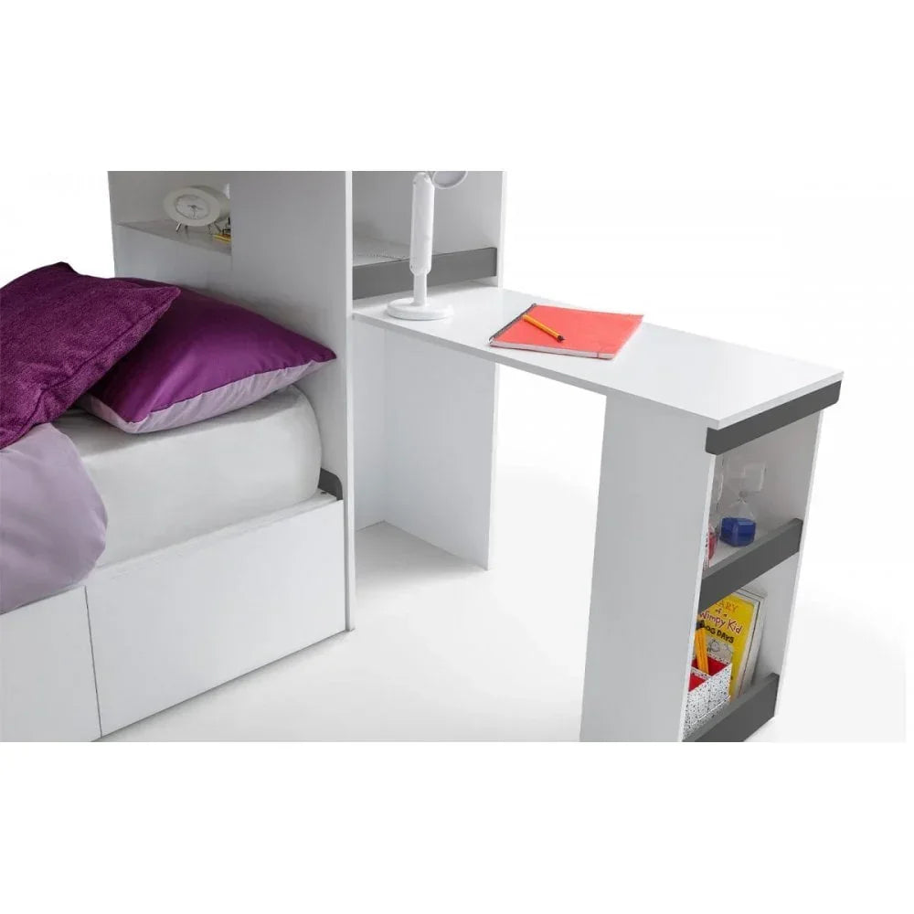White desk with built-in shelves beside bed, purple pillows, lamp, and stationery visible