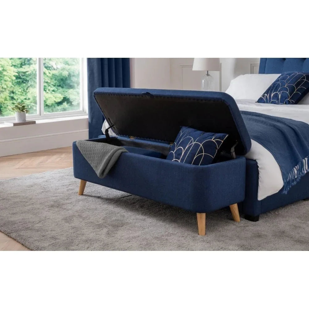 Blue fabric ottoman storage bench at end of bed with wooden legs and soft close lid