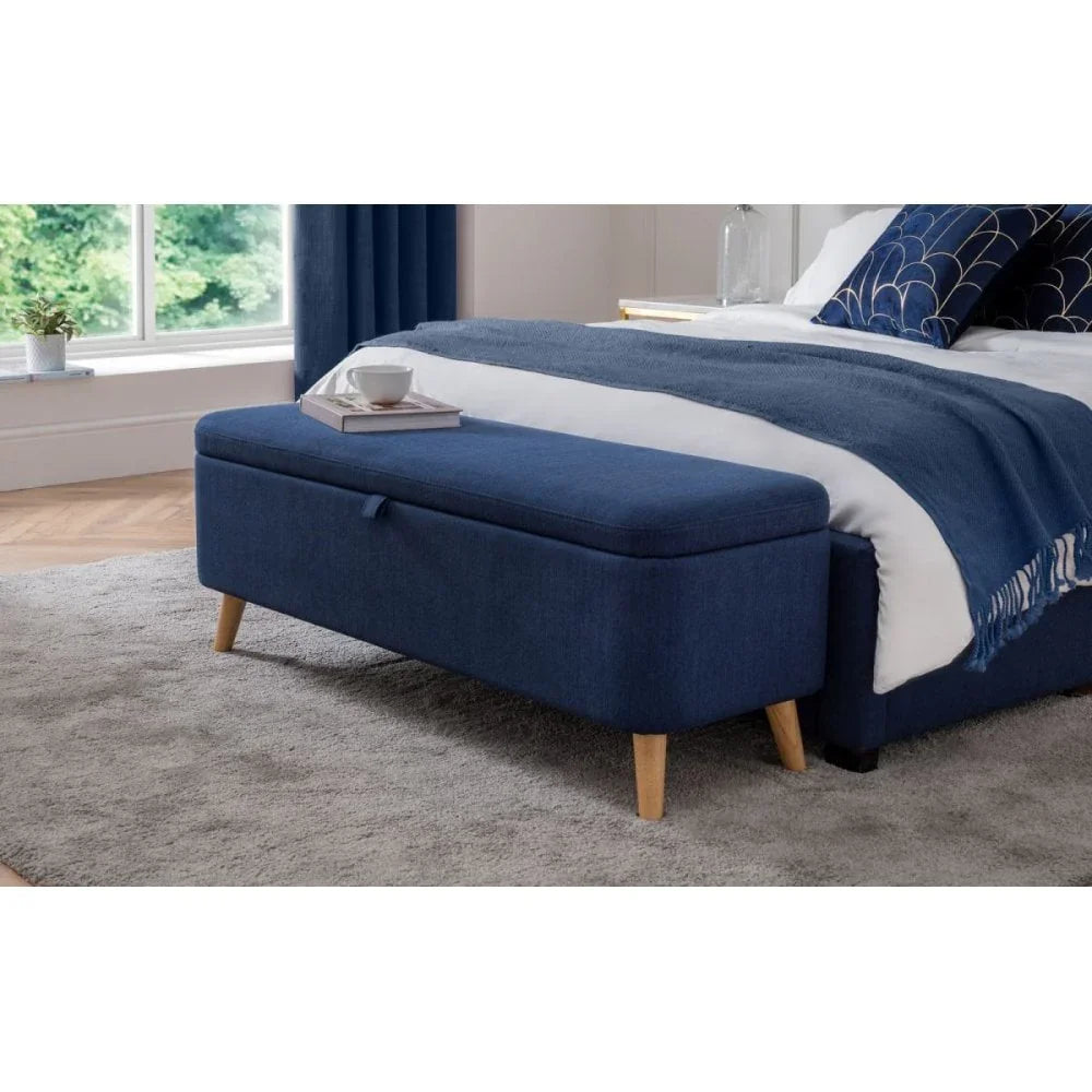 Blue storage ottoman bench with wooden legs at foot of bed in modern bedroom