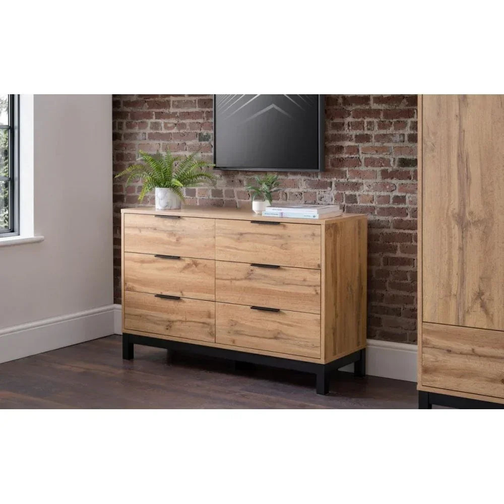Oak wood chest of drawers with black handles in modern bedroom setting