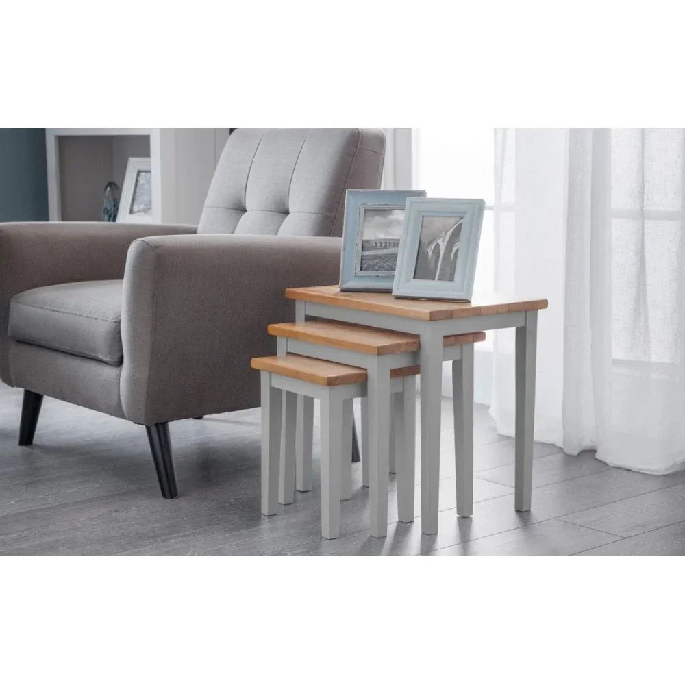 Grey nesting tables with wooden tops beside grey armchair, photo frames displayed on top