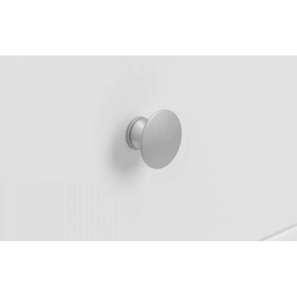 Closeup of round silver drawer handle on smooth white furniture surface