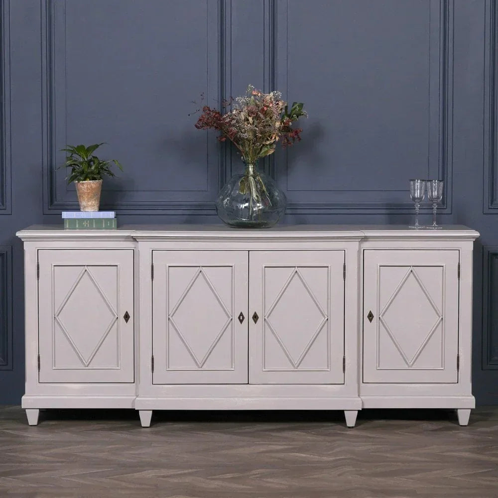 White sideboard cabinet with diamond panel doors, vase, plant and glassware on top