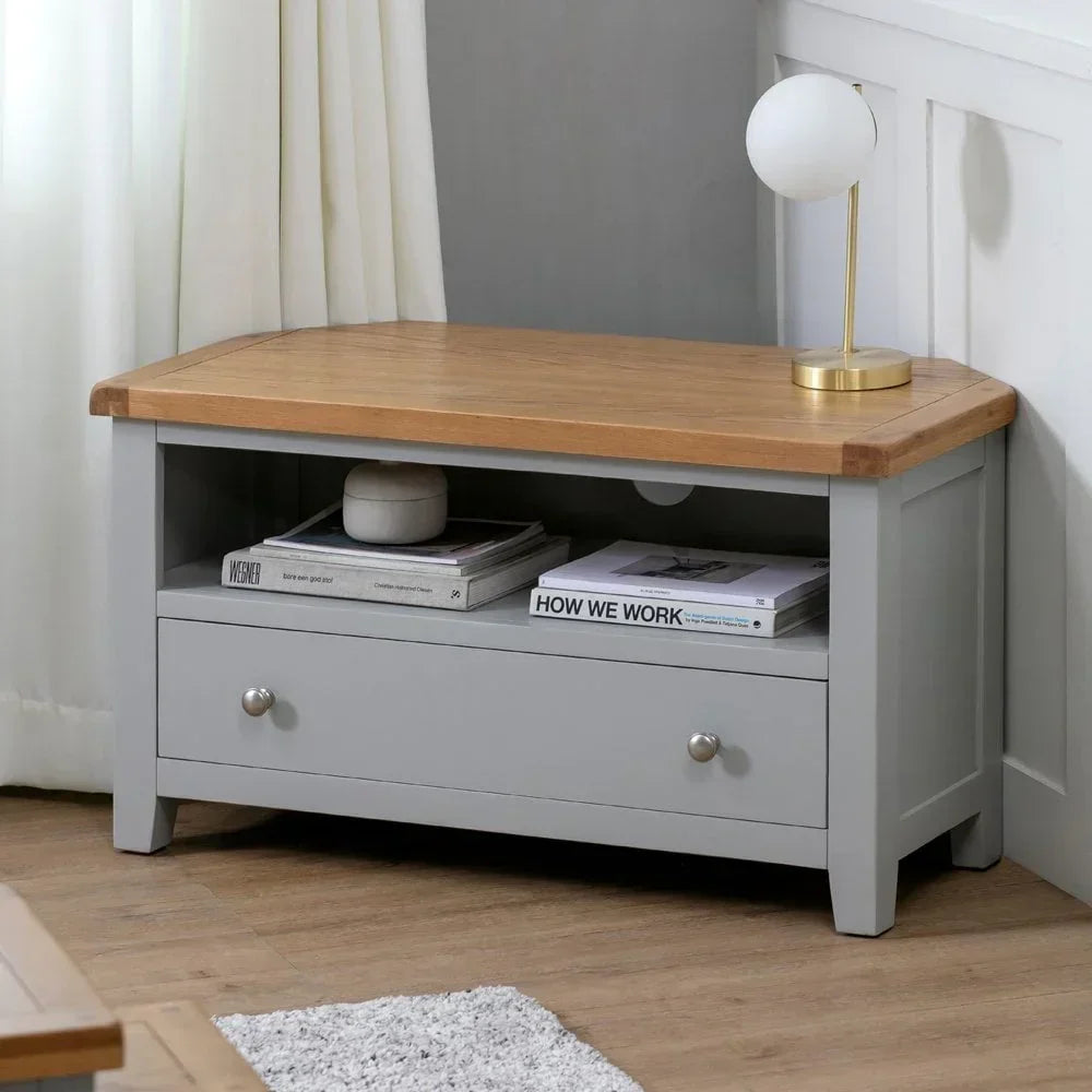Grey wooden TV unit with oak top, single drawer, open shelf holding books, table lamp on top