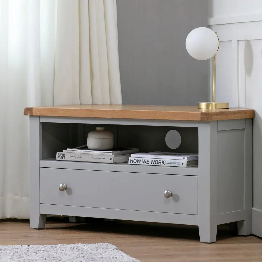 Grey wooden TV unit with oak top, drawer, open shelf, books and table lamp
