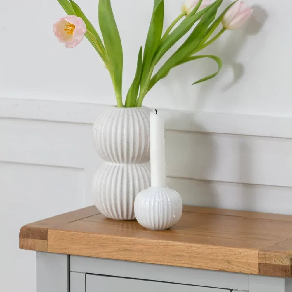 White ribbed ceramic vase with pink tulips and matching candle holder on wooden sideboard