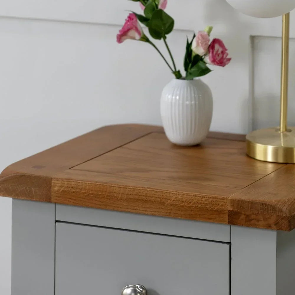 Grey bedside table with oak top, metal knob, white vase and lamp on surface