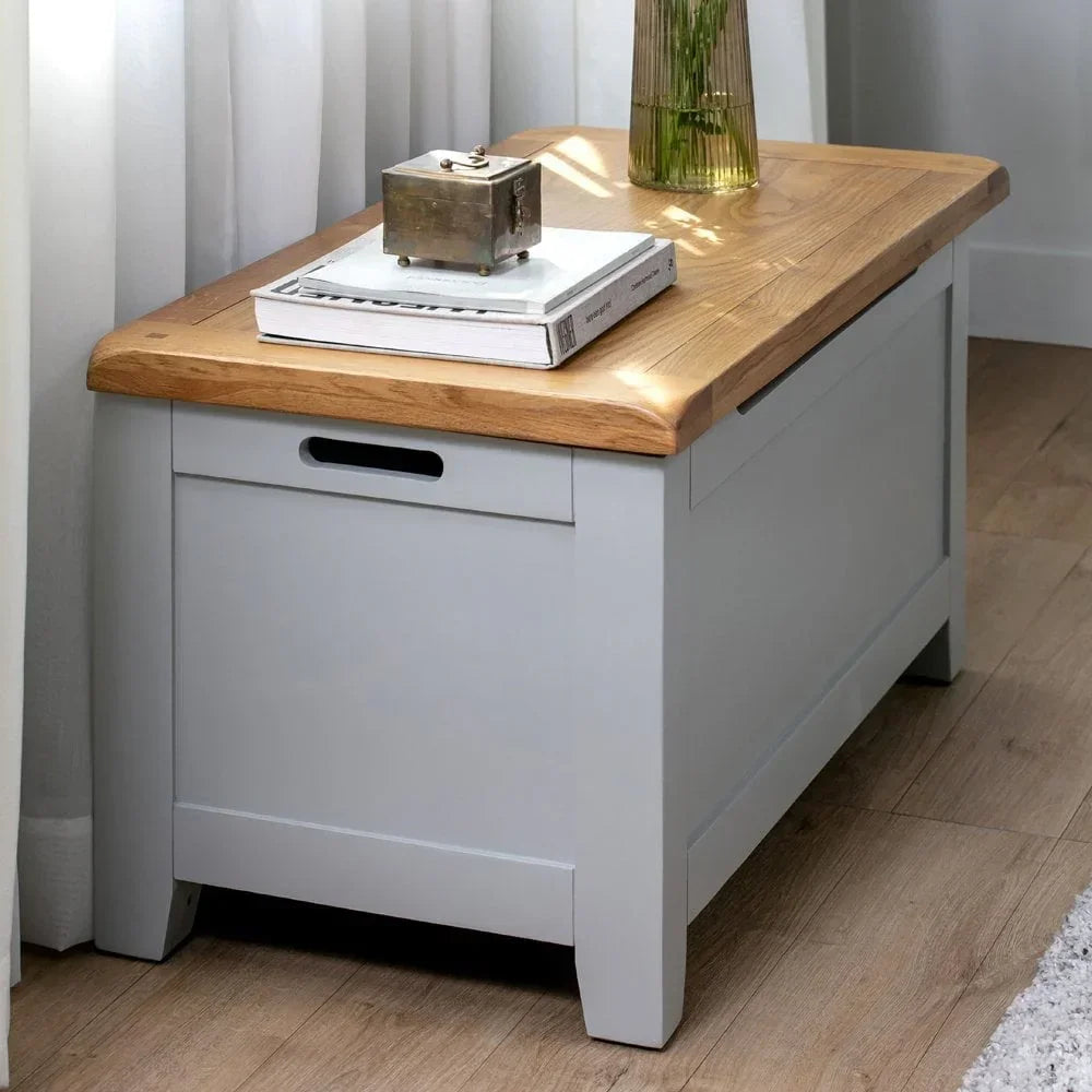 Grey wooden storage bench with oak top placed in living room next to window