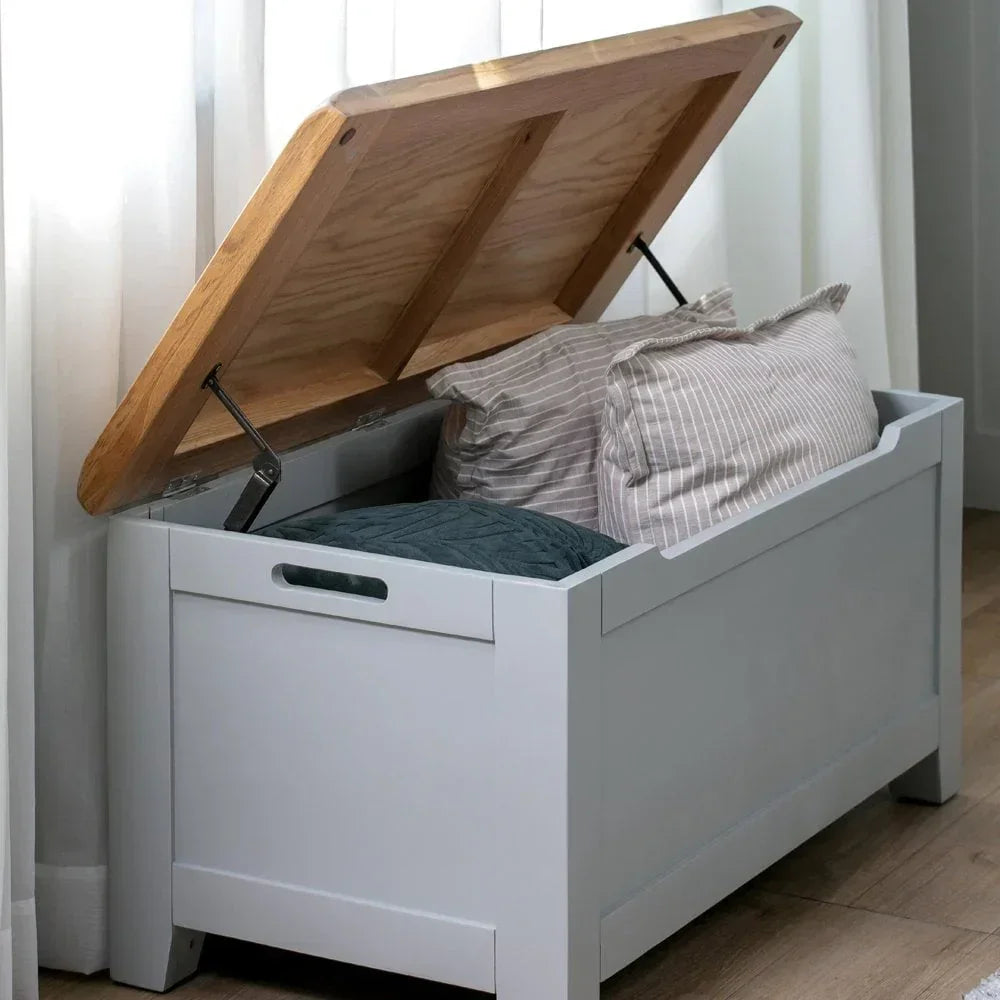 Wooden storage bench with open lid holding pillows in a bright room