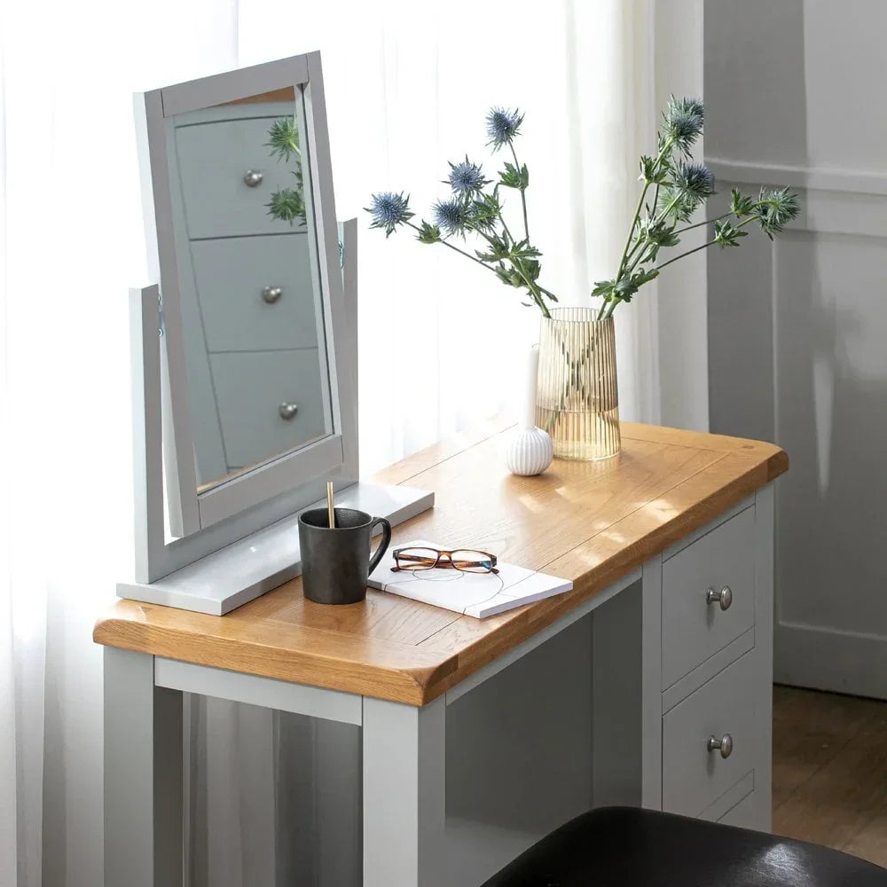 Oak and grey dressing table with mirror, glass vase, and drawers in bright room