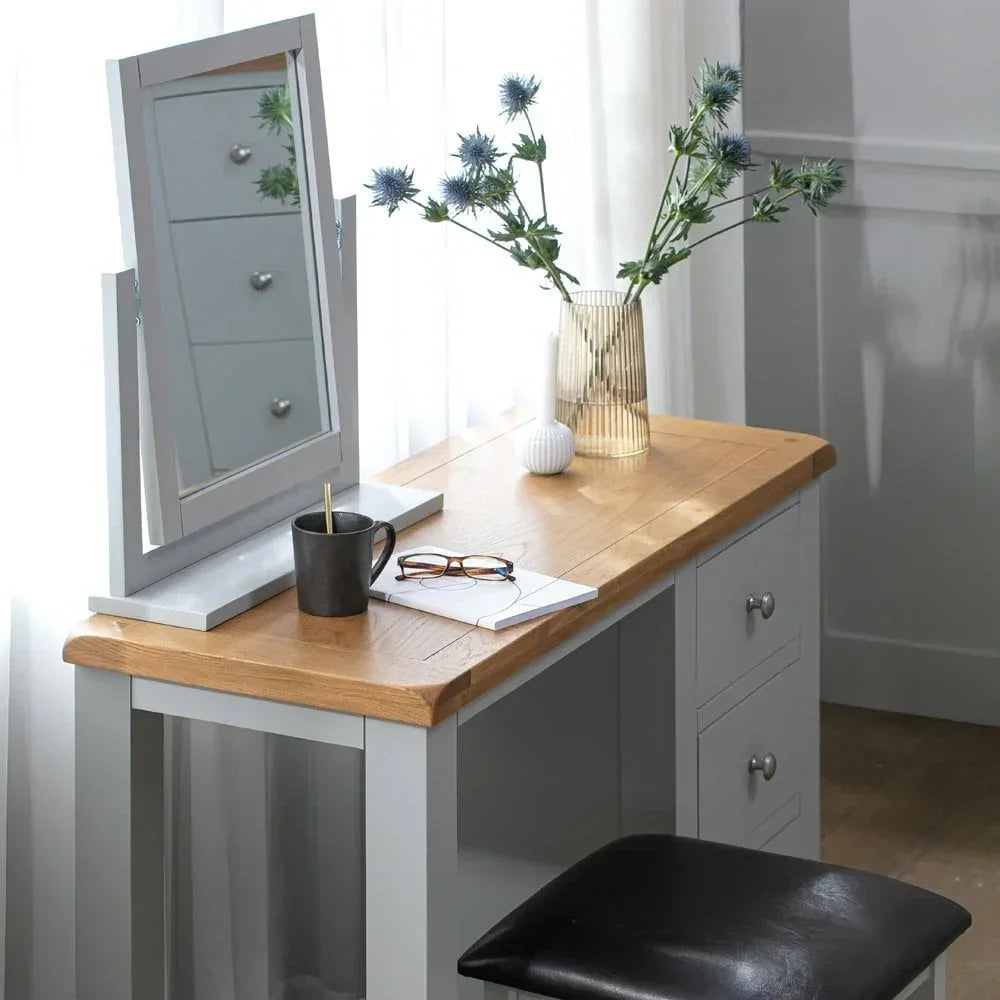Grey and oak dressing table with mirror, drawers, black stool, and vase with flowers