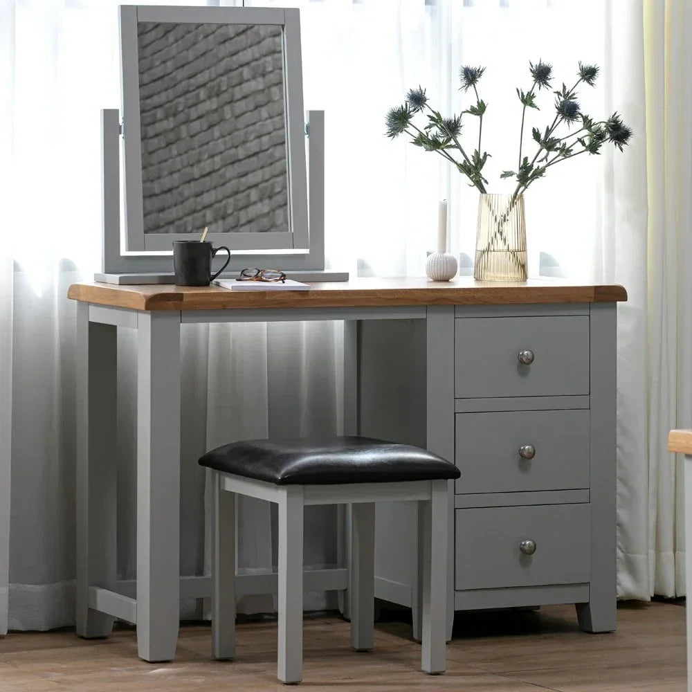 Grey wooden dressing table with mirror, matching stool, and three drawers in natural light