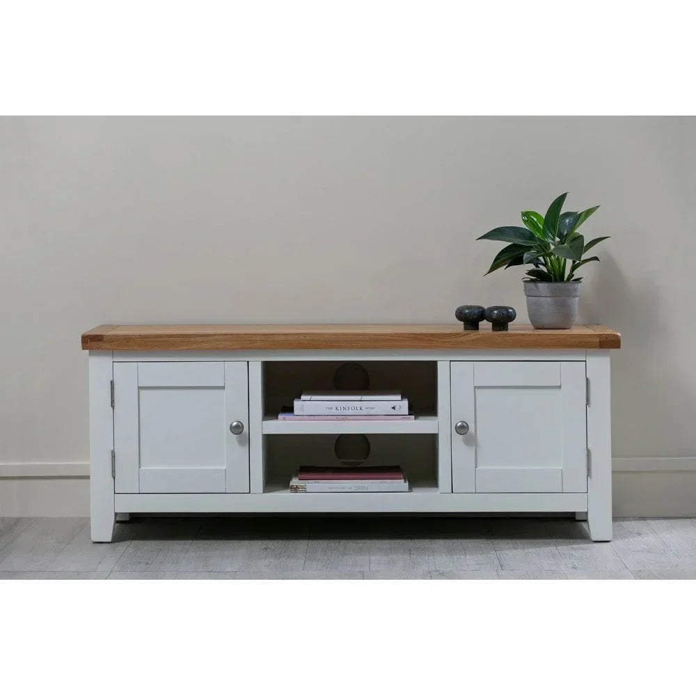 White wood TV unit with oak top, two doors, shelving, books and a potted plant