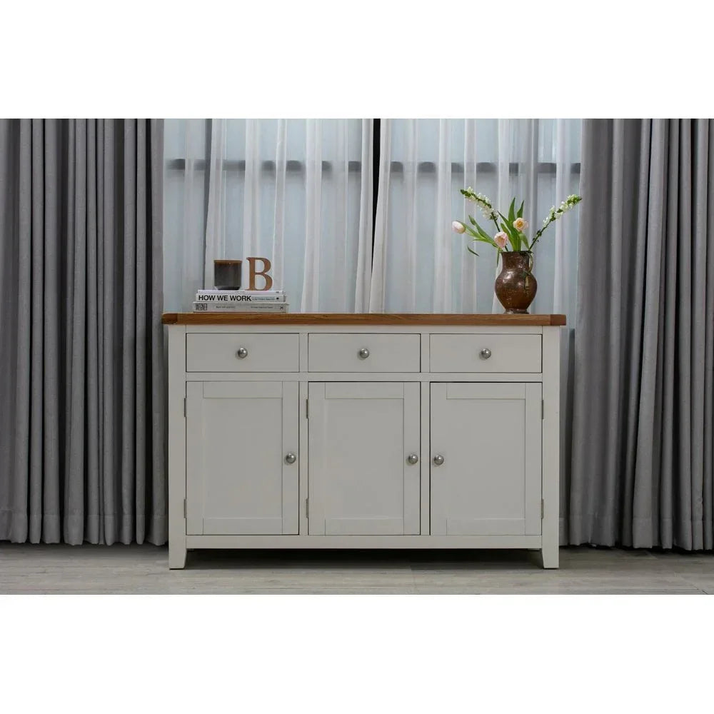 White sideboard with wooden top, three drawers and cabinet doors, vase and books on top