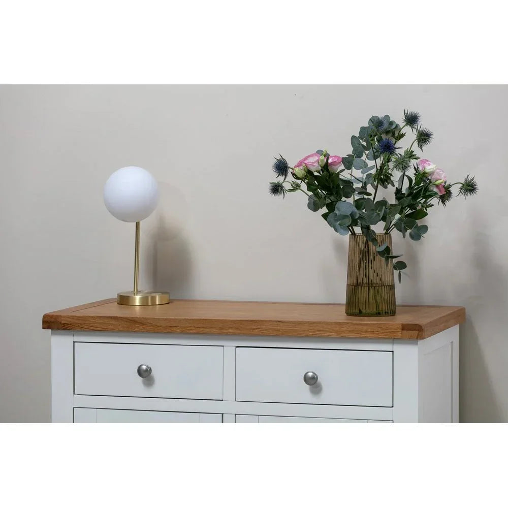 White and oak sideboard with drawers, topped with gold lamp and glass vase of flowers