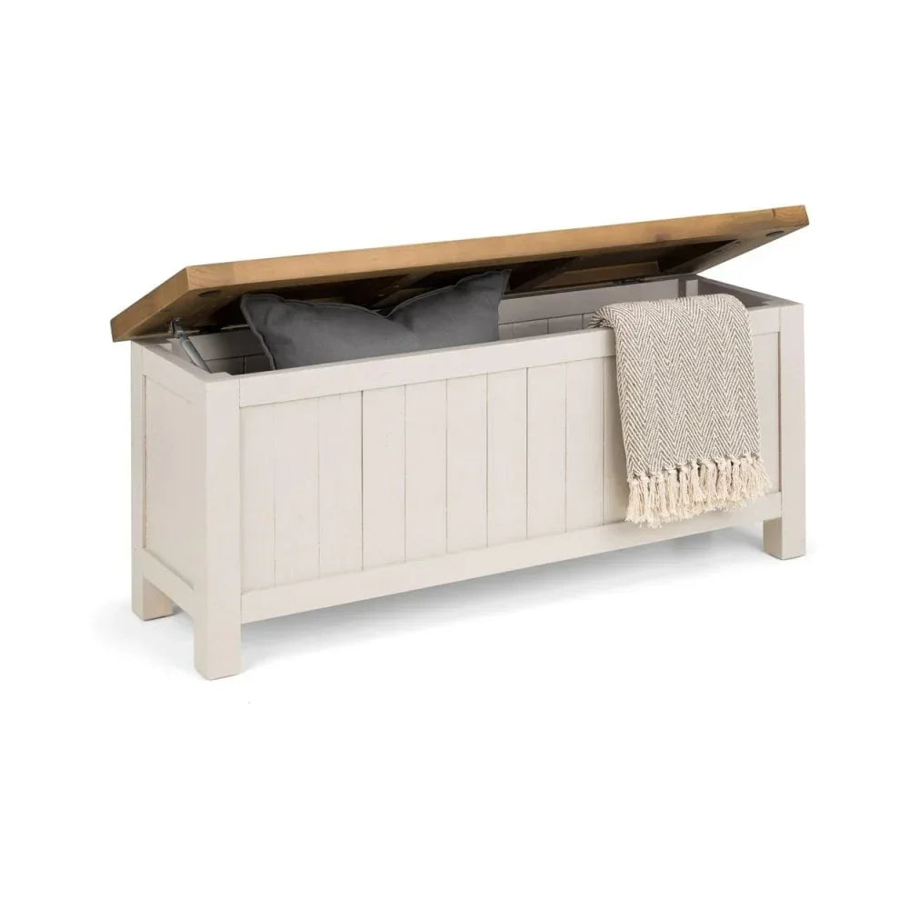 Wooden storage bench with open lid, two grey cushions and a throw draped over the side