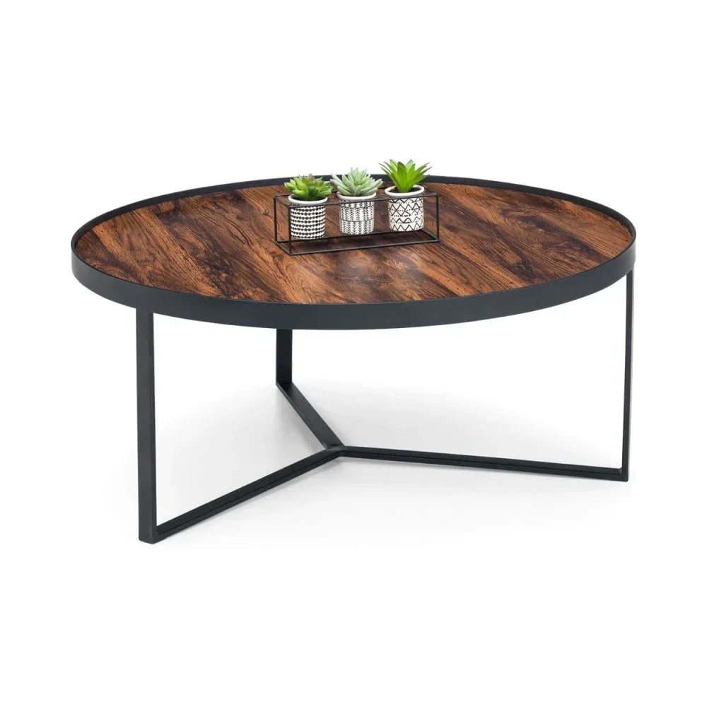 Round industrial coffee table with dark wood top, black metal legs, and small plant decor