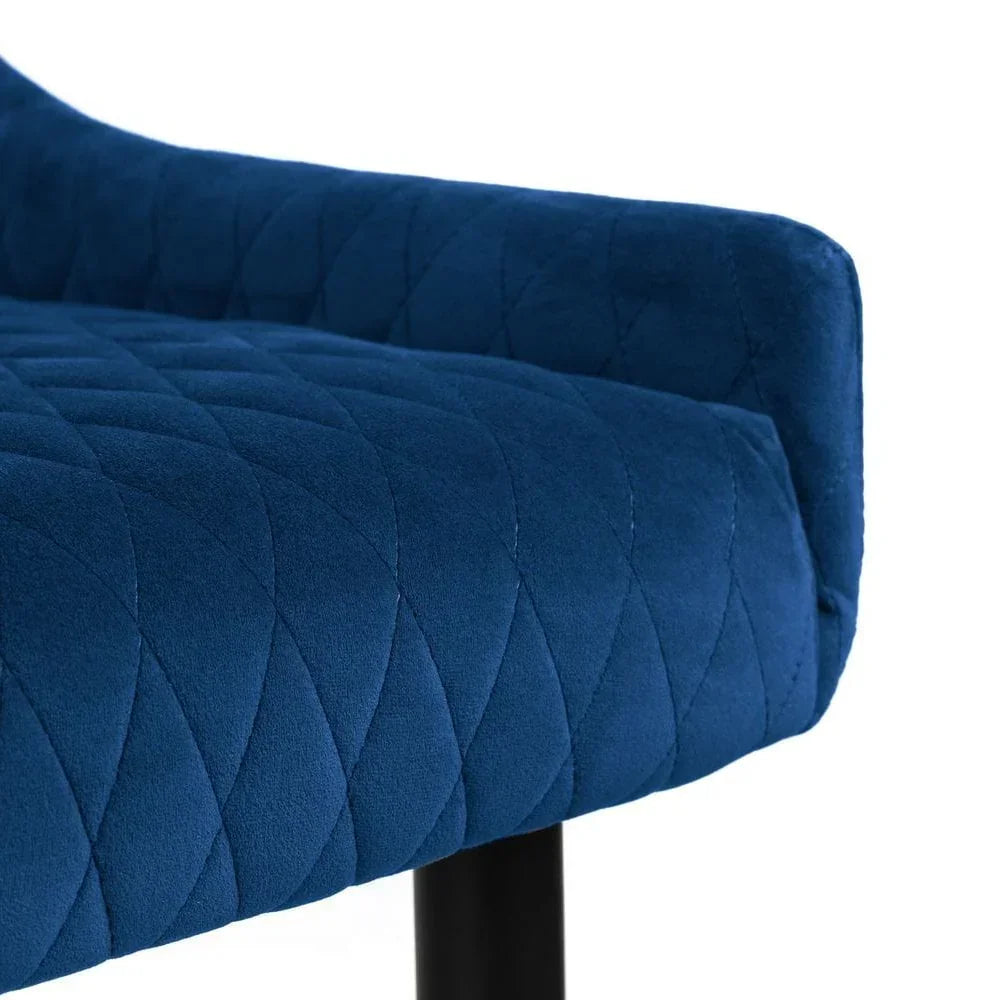 Blue velvet dining chair closeup with quilted seat and armrest, black metal leg visible