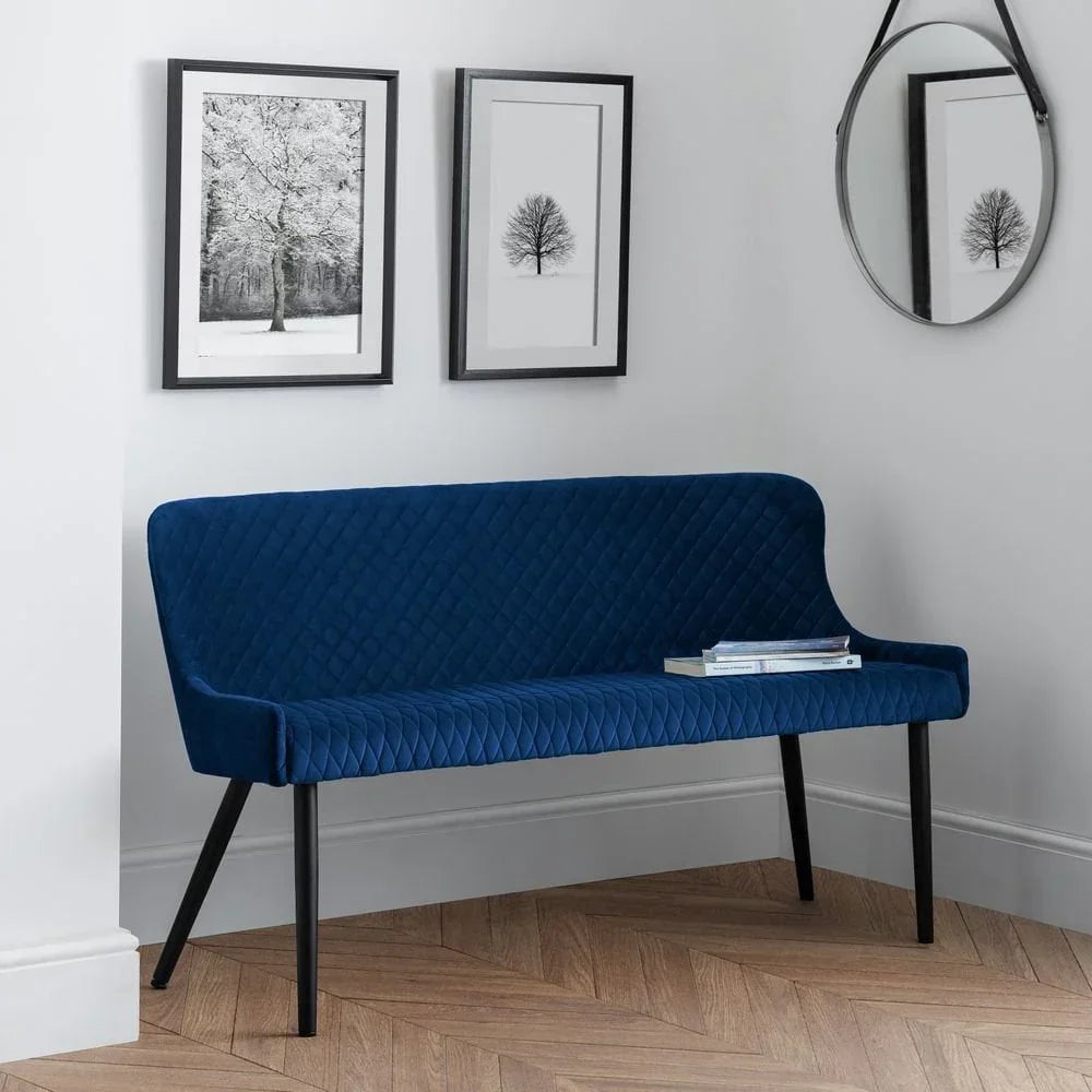 Blue velvet dining bench with diamond stitching and black legs against white wall