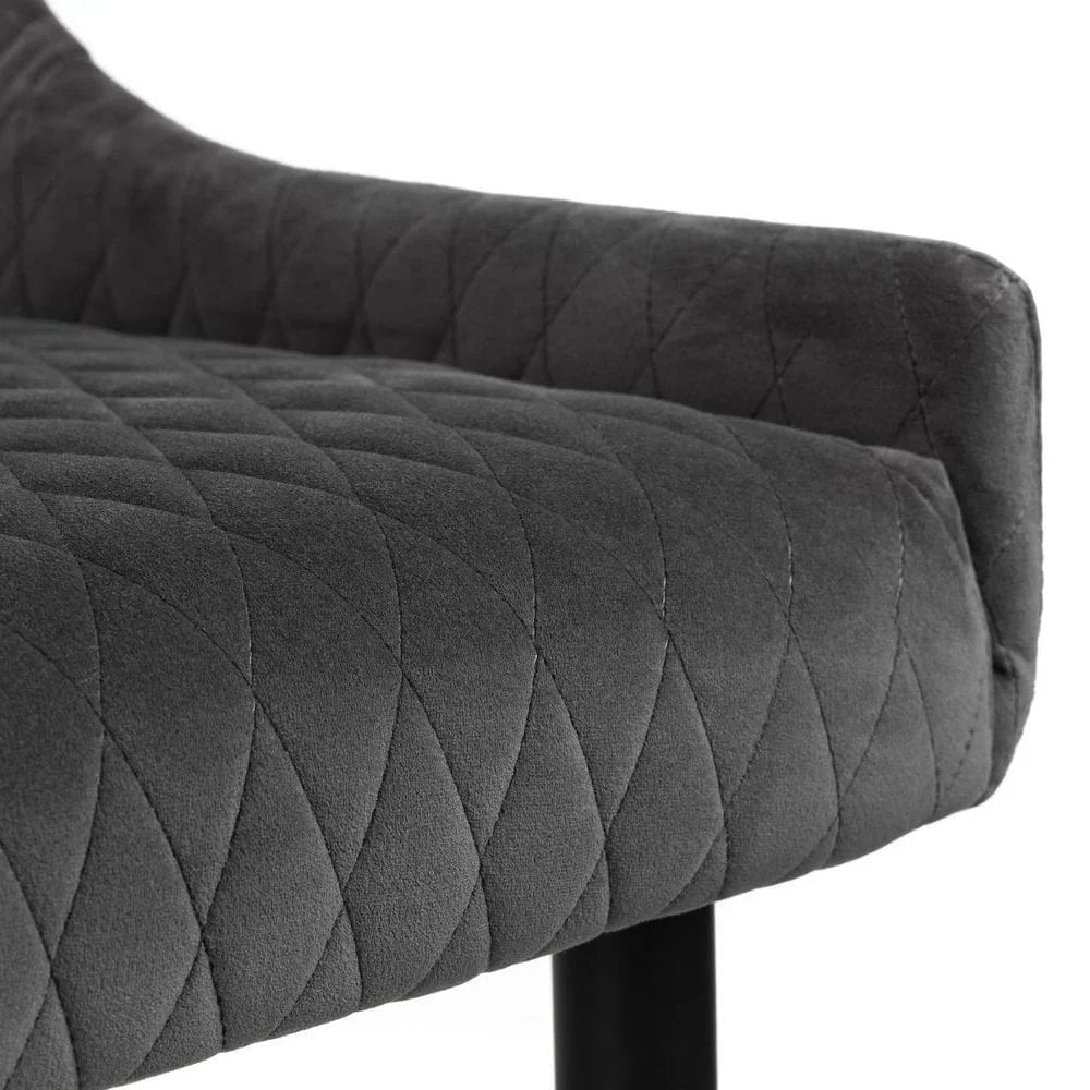 Closeup of grey upholstered dining chair seat with quilted stitching and black metal leg