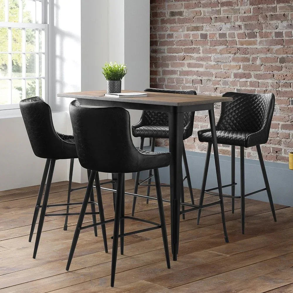 Black bar stools with quilted backs around a tall wood dining table in loft-style room